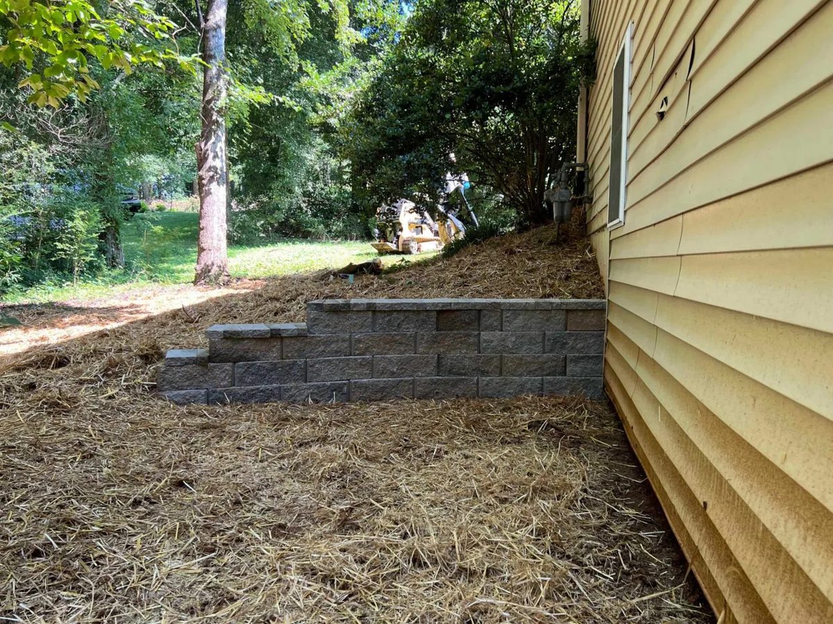 Retaining wall and regraded slope alongside a house foundation